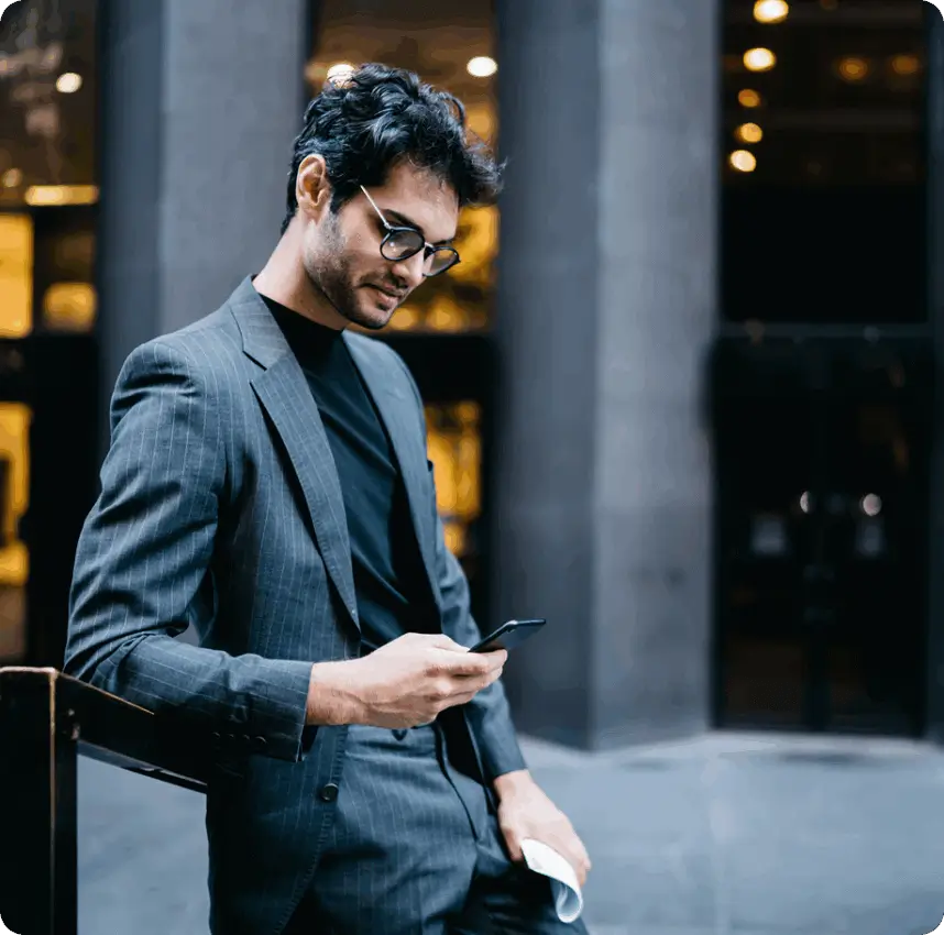 Man in a jacket checking his phone while standing outside a building in an urban setting.