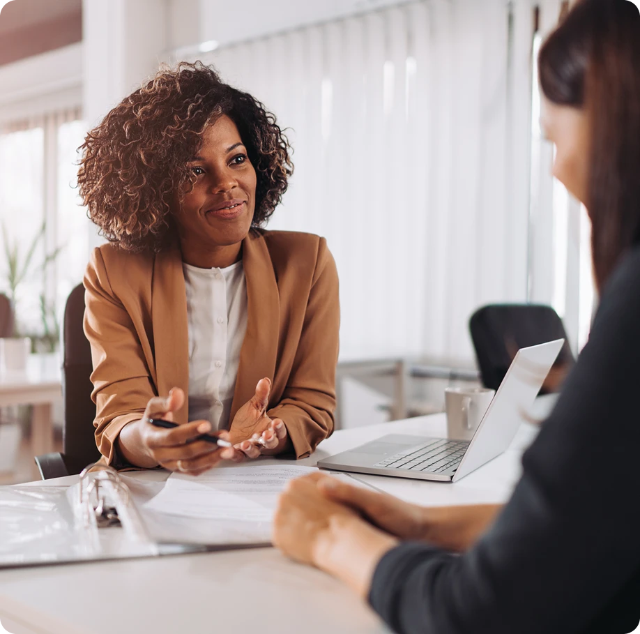 Customer and agent discussing documents with a laptop open between them.