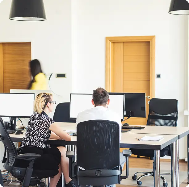 Coworkers collaborating on a desktop computer in an open office.